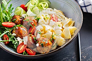 Conchiglie with meatballs, feta cheese and salad on dark background.