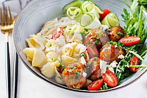 Conchiglie with meatballs, feta cheese and salad on light background.