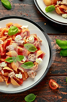 Conchiglie Tuna pasta with tomato sauce, feta cheese and basil on wooden table. healthy food