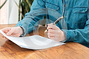 Conclusion of the contract. A woman in a denim shirt is sitting at a table, holding documents and a pen in her hands
