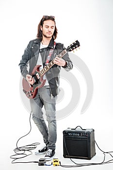 Concntrated young male guitarist playing electric guitar and using amplifier