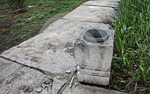 Concrete and aluminum trash and garbage can next to the damaged path in the park.