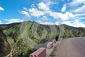 Concrete barriers by asphalt road turn with lush green mountain forests in the background