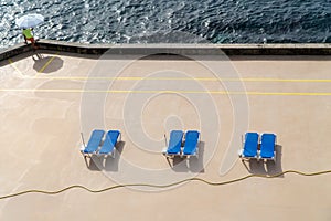 Concrete beach with tree couple of blue deck chairs under the sun light, Madeira island, Portugal