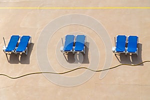 Concrete beach with tree couples of blue empty deck chairs under the sun light, Madeira, Portugal