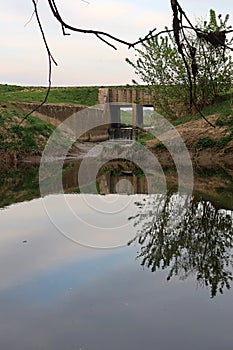 Concrete bridge with confluence of artificial water channel with Nitra river under it, as viewed from opposite bank.