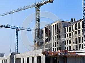 Concrete building construction site with cranes in blue sky