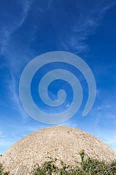 A concrete building , which looks like the spherical surface of the moon rises over the bright blue sky with clouds