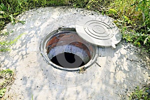 Concrete cesspit with an open hatch on the ground in the summer