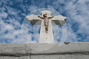 Concrete christian cross with brass Jesus on blue cloudy sky.