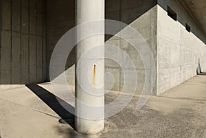 Concrete column on cement sidewalk with solid reinforced concrete wall on behind