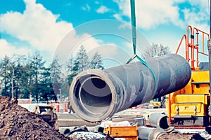 Concrete drainage pipe lifted by excavator during deep drainage works on construction site