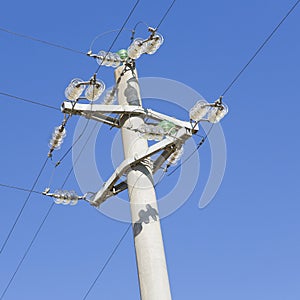 Concrete electricity pylon against a blue background with copper electrical cables and glass insulators