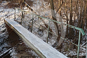 Concrete footbridge with green rusty metal railings, forest, winter