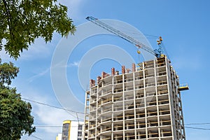 Concrete frame of tall apartment building under construction and tower crane in a city