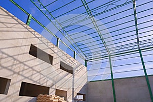 Concrete industrial office building structure with green metal roof beam and column of warehouse outline against blue sky