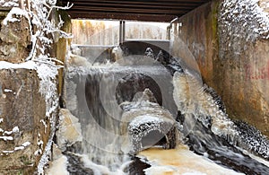 Concrete lake weir with non-freezing water stream in winter