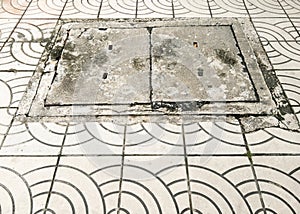 The concrete manhole cover on the pavement of the brick way