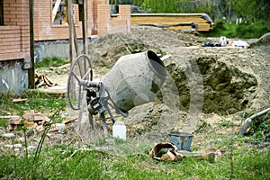 Concrete mixer in construction. Cement mixer at a construction site, tools, a pile of sand and a bucket