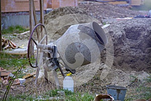 Concrete mixer in construction. Cement mixer at a construction site, tools, a pile of sand and a bucket