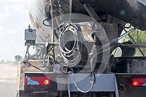 Concrete mixer truck rear view with hoses and burning taillights during road works on an intercity highway