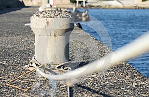 Concrete mooring bollard with a rope at a dock.