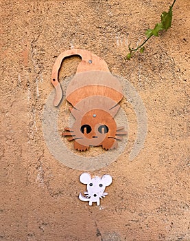 a concrete orange wall with orange wooden cat running after a white mouse, funny orange cat chasing a scaredy white mouse in a