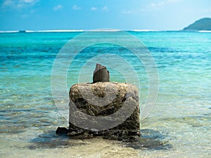 Concrete outcropping with remains of a wooden pillar off a Seychelles beach under blue sunny skies.