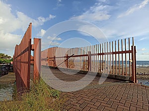 Concrete outdoor bridge with red fences on blue summers sky background over the beach.