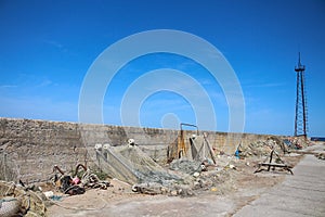 A concrete pier that goes out to sea, with fishing nets on it, and a derrick at the end. Against a bright blue sky with feathery