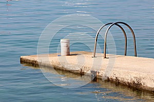 Concrete pier with partially rusted metal handrails for easier entrance and mounted metal hook for tying small boats