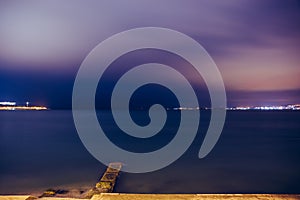 Concrete pier after sunset in sea water, night landscape with harbor and ocean