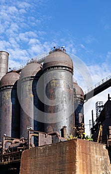 Concrete pillars and blast furnaces of an old steel mill plant, bright blue sky and clouds