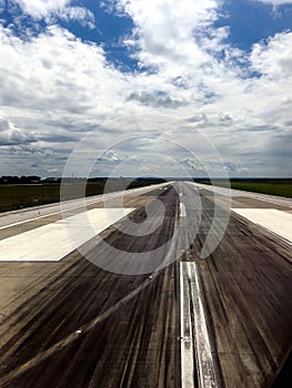 Concrete runway in diminishing perspective with black tire marks and white paint lines in green airfield