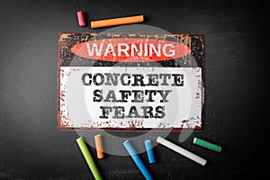 Concrete safety fears. Metal warning sign and colored pieces of chalk on a dark chalkboard background