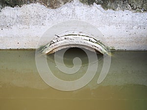 Concrete sewer pipe under embankment with dirty sewage flooded