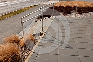Concrete staircase with stainless steel polished tubular railing. cobblestones cobblestones concrete. colorful bushes of red color