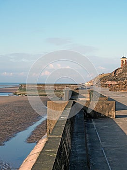 Concrete stairs on seawall in blackpool with the beach at low tide in sunlight with the old boat pool and tower in the difference