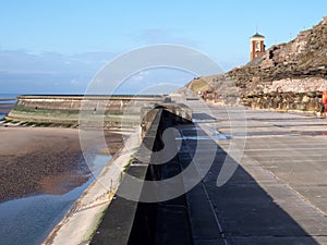 Concrete stairs on seawall in blackpool with the beach at low tide in sunlight with the old boat pool and tower in the difference