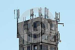 Concrete tall dilapidated old rarely used industrial building with densely mounted cell phone antennas and transmitters on top