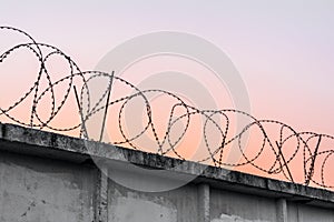 Concrete wall with barbed wire against a blue orange evening sky