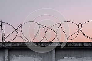 Concrete wall with barbed wire against a blue orange evening sky