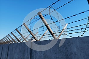 Concrete wall with barbed wire against blue sky. Concept border, prisons, refugees, loneliness. 3D illustration, 3D render, copy