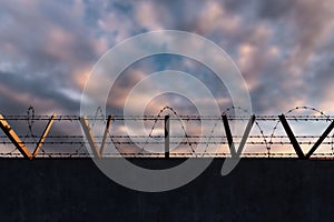 Concrete wall with barbed wire against blue sky. Concept border, prisons, refugees, loneliness. mixed media, copy space