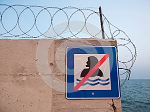Concrete wall with barbed wire atop and sign Swimming prohibited