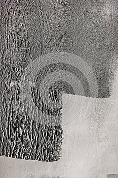 Concrete wall partially painted in gray with a paint roller. Paint texture in side sunlight