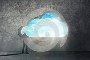 Businessman standing on concrete floor and looking to sky thru cloud shape hole on concrete wall.