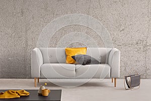 Concrete wall in trendy living room interior with grey scandinavian sofa, newspaper rack and coffee table with yellow cloth,