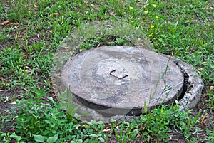 Concrete water manhole in the grass, a concrete well on the background of grass