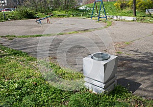 Concrete white trash can on the green grass next to asphalt area of playground in the park.